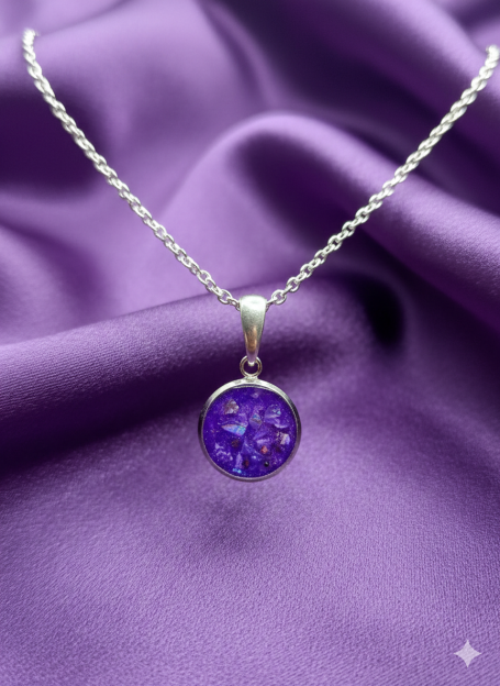 Silver necklace with a round purple gemstone pendant on a purple fabric background.